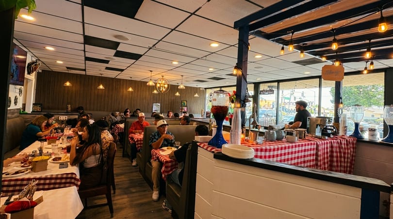 A bustling restaurant interior with patrons dining at tables covered in red and white checkered tablecloths.