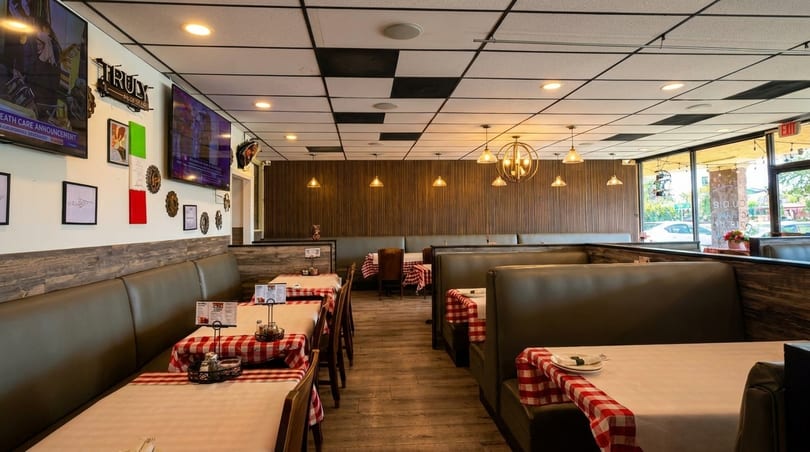 Restaurant interior with booth seating, red and white checkered tablecloths, and wall-mounted TVs.