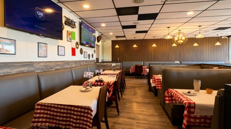 Empty restaurant dining room with booths, tables with red and white checkered tablecloths, and wall-mounted TVs.